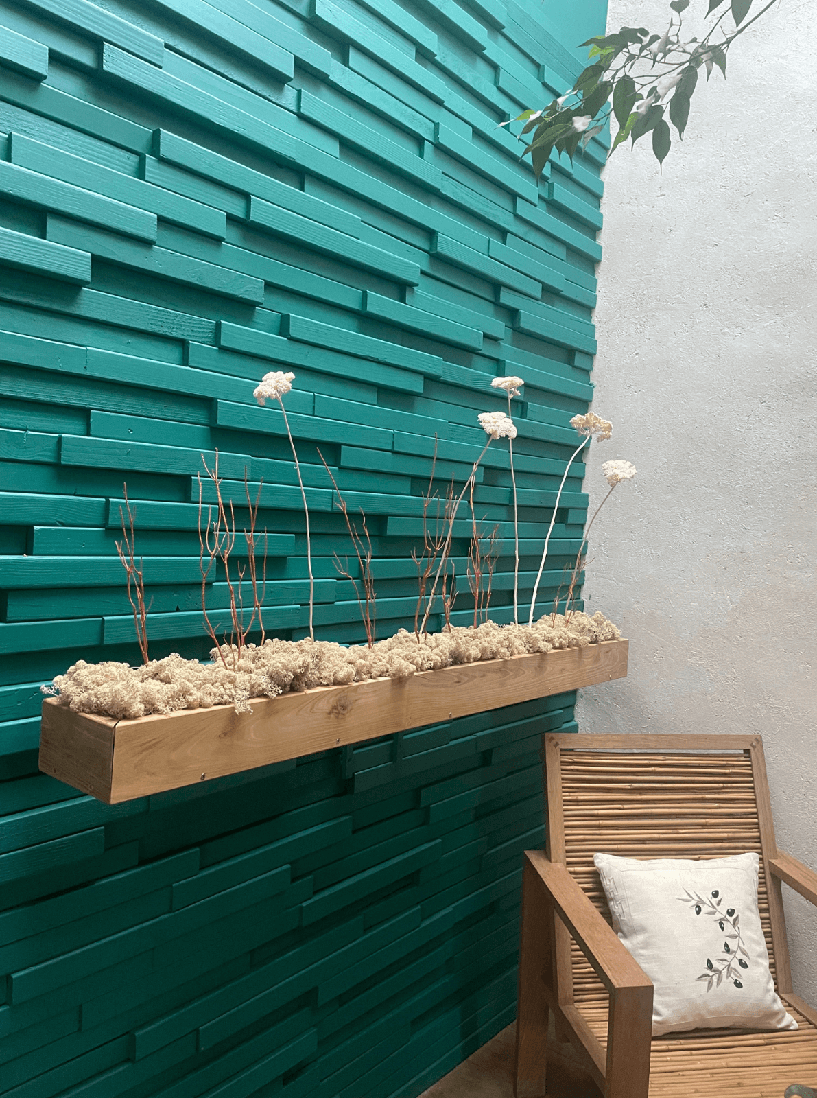 Décoration intérieure au design floral en lichen stabilisé et plantes naturelles stabilisées dans une maison contemporaine. Composition en végétaux stabilisés accroché à un mur turquoise en bois, avec une chaise en bambou.