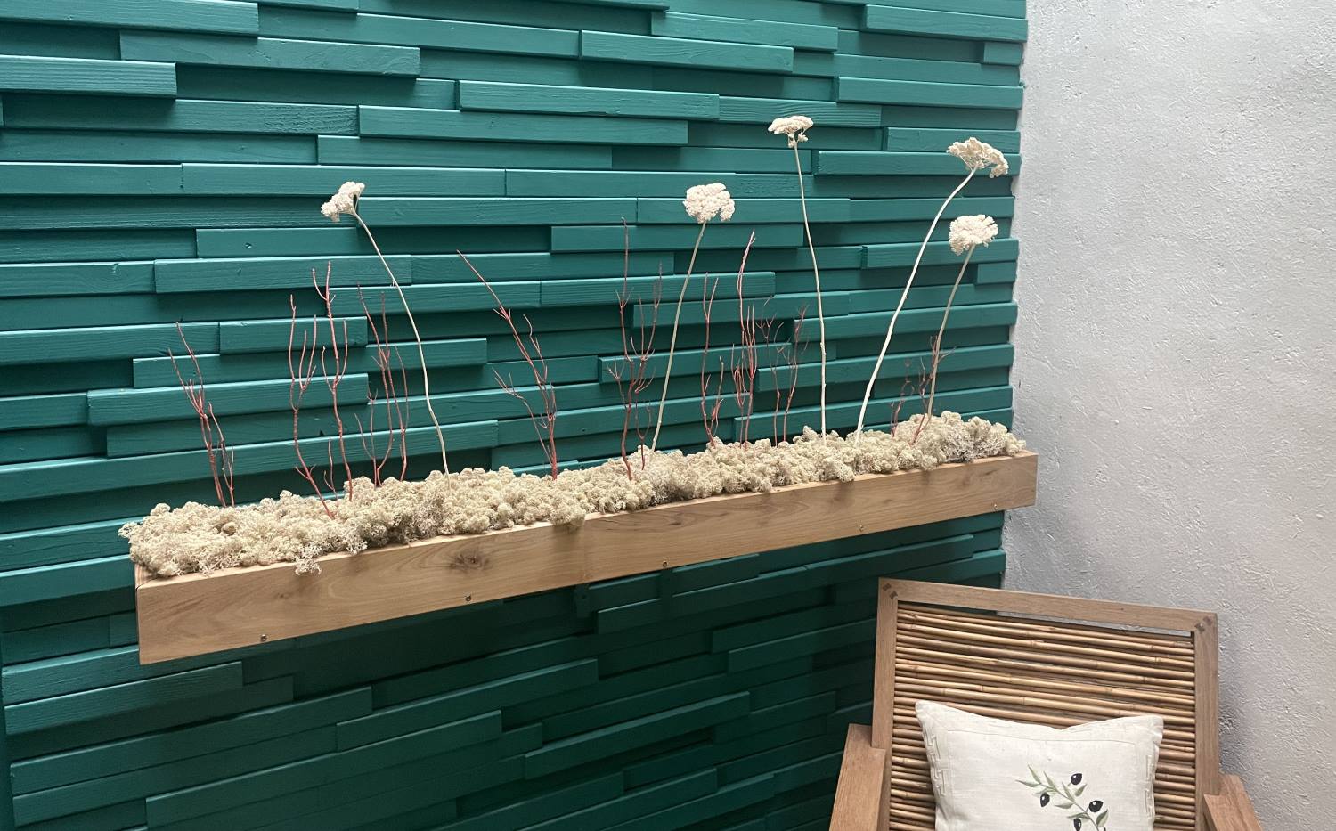Décoration intérieure au design floral en lichen stabilisé et plantes naturelles stabilisées dans une maison contemporaine. Composition en végétaux stabilisés accroché à un mur turquoise en bois, avec une chaise en bambou.