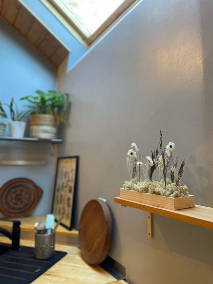 Décoration intérieure au design floral en lichen stabilisé et plantes naturelles stabilisées dans une maison contemporaine. Composition en végétaux stabilisés posé sur une étagère dans une cuisine moderne. La composition est sur les tons naturels.