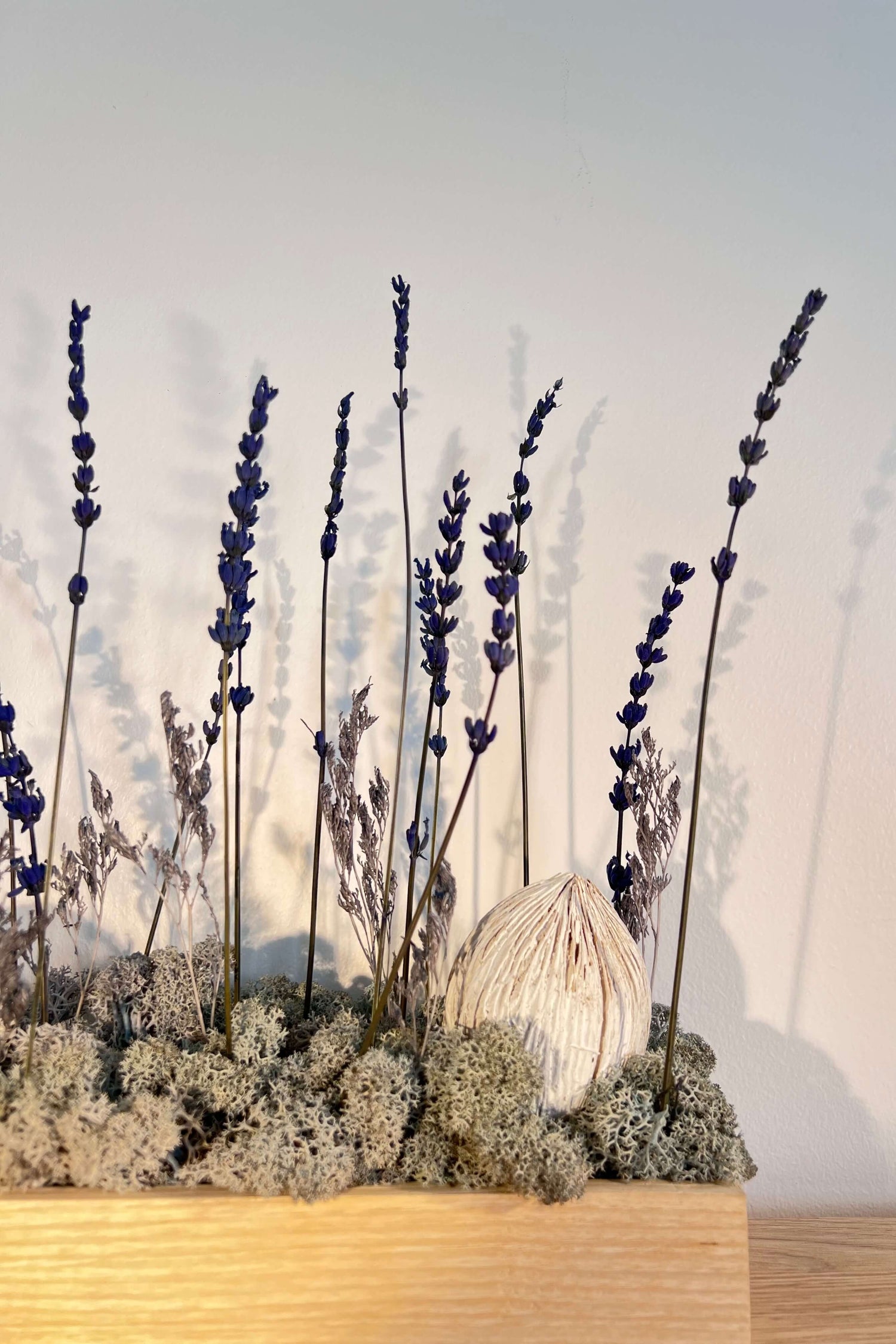 Composition florale avec un support en bois massif posé sur une table en bois. Le lichen stabilisé est bleu et avec de la lavande et autre feuillage.
